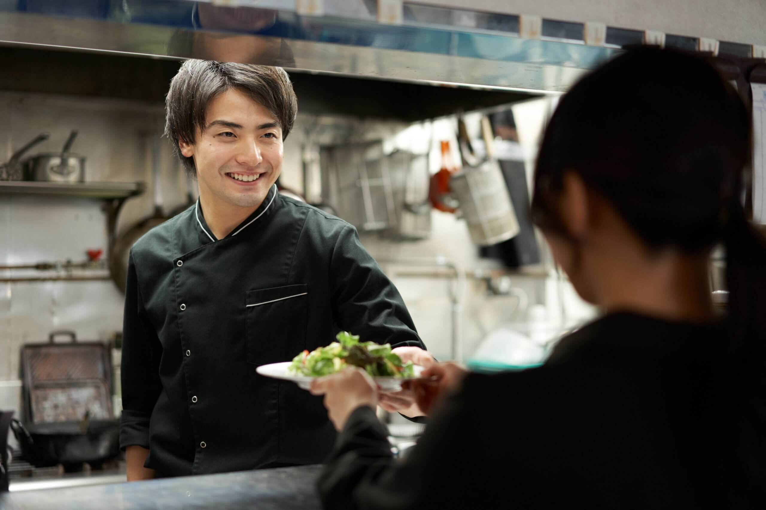 a chef handing over a dish to the waiter in a positive and happy work environment