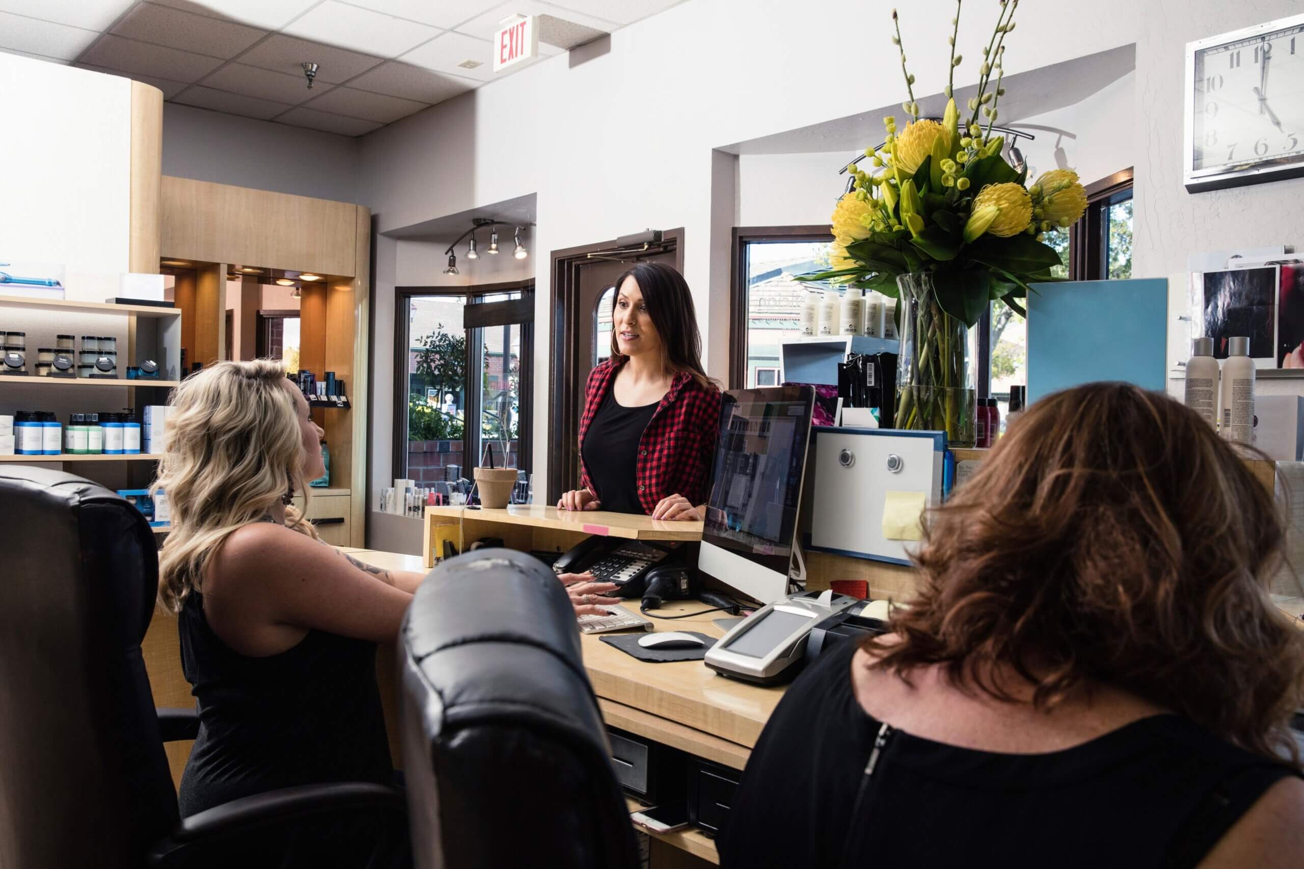 Three employees working and discussing at the front counter of a tanning salon, with a tanning salon software in use
